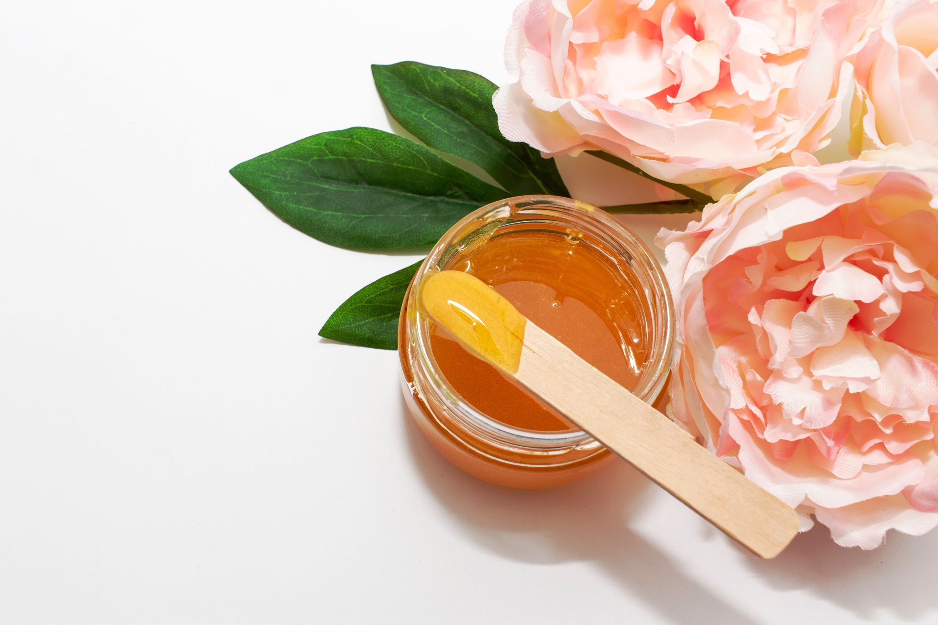 Liquid sugar paste for hair removal in a bowl with peony flower on white background.